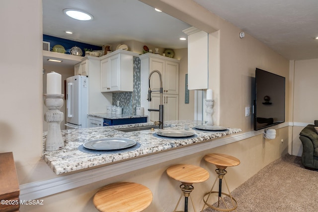 6951 E Hayne Pl, Tucson, AZ 85710 - kitchen featuring freestanding refrigerator, white cabinetry, light stone counters, a breakfast bar area, and recessed lighting