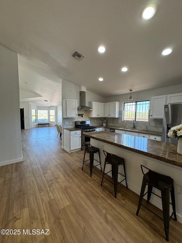 1129 W Amberbrooke Ave, Tucson, AZ 85745 - kitchen with appliances with stainless steel finishes, wall chimney exhaust hood, a breakfast bar area, backsplash, and wood finished floors