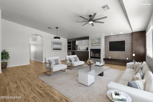 446 Soda Ln, Rio Rico, AZ 85648 - living area with arched walkways, a ceiling fan, wood finished floors, built in shelves, and a fireplace