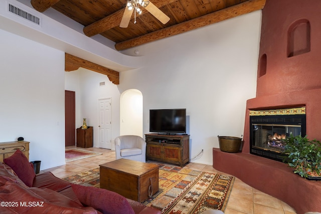 10380 E Rancho Del Este Dr, Tucson, AZ 85749 - living area with a wooden ceiling with exposed beams, arched walkways, ceiling fan, tile patterned flooring, and a glass covered fireplace