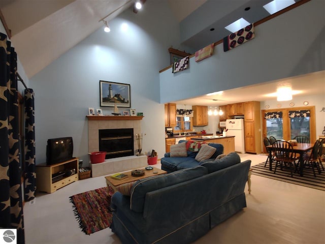 living room featuring track lighting, light colored carpet, a tiled fireplace, and a high ceiling