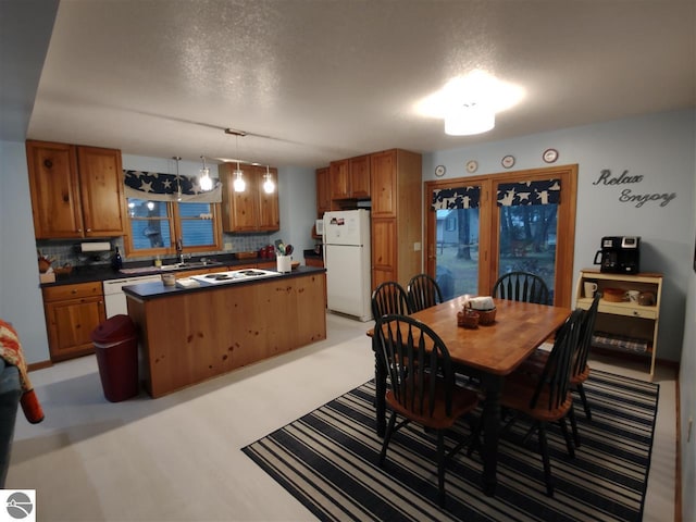 kitchen with sink, white appliances, hanging light fixtures, backsplash, and a center island