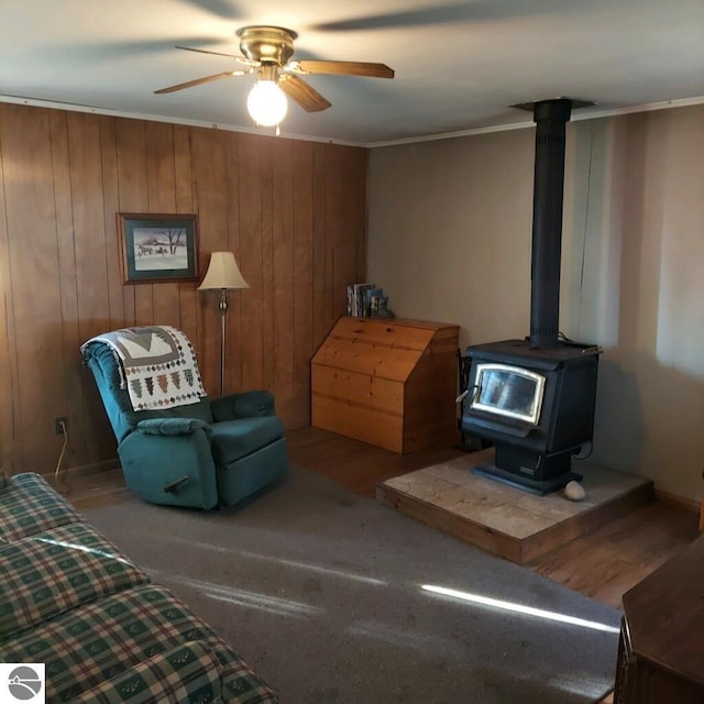 sitting room featuring a wood stove, crown molding, ceiling fan, and wood walls