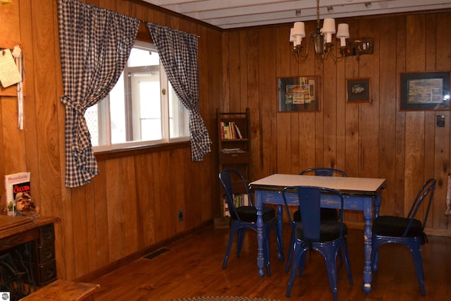 dining space with wooden walls, an inviting chandelier, and dark hardwood / wood-style floors