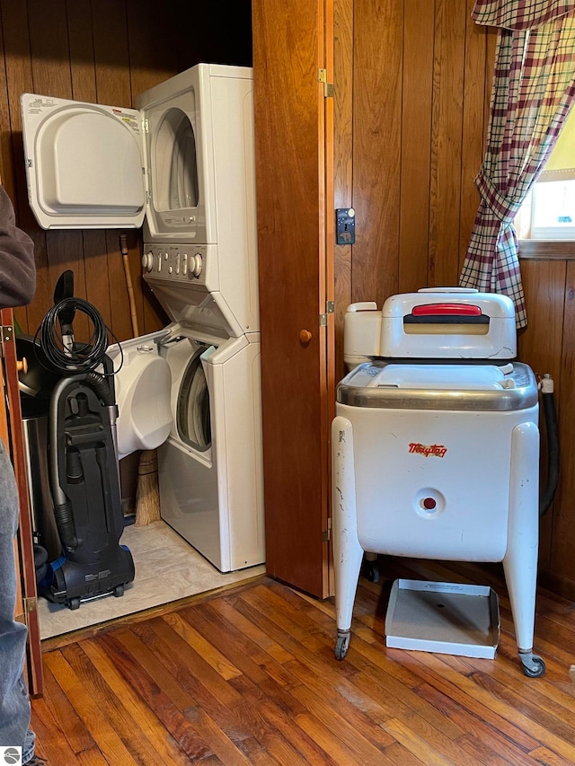 laundry area featuring wooden walls, stacked washer / drying machine, and wood-type flooring