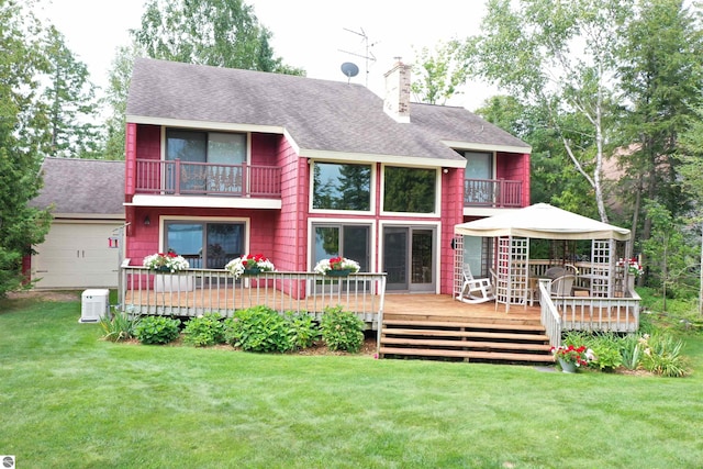 back of property featuring a balcony, a wooden deck, and a lawn