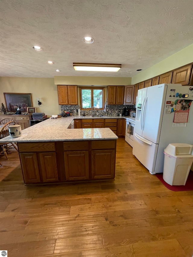 kitchen with electric range oven, white refrigerator with ice dispenser, light hardwood / wood-style flooring, and kitchen peninsula