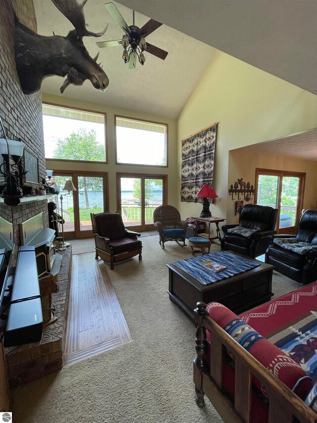 carpeted living room featuring ceiling fan, high vaulted ceiling, brick wall, and a brick fireplace