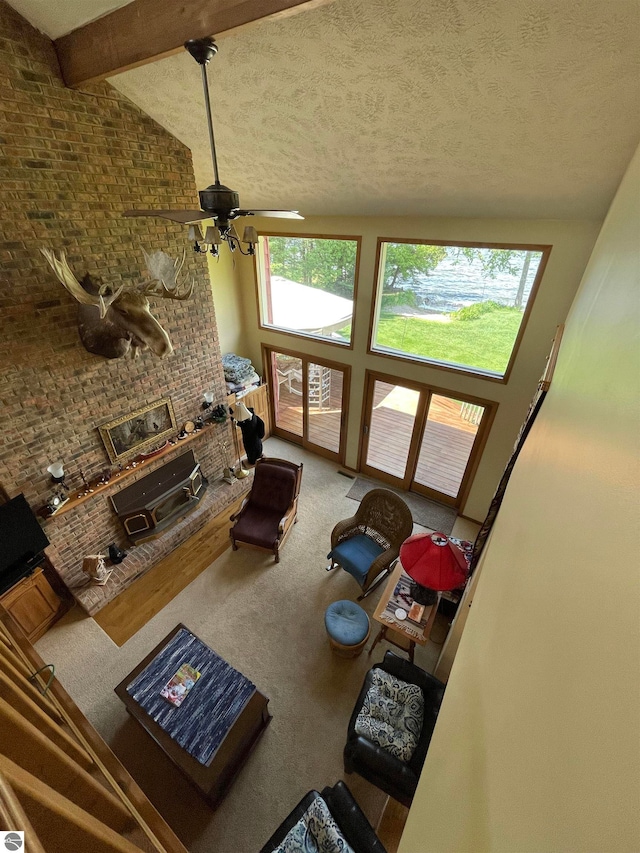 living room with a fireplace, ceiling fan, a textured ceiling, carpet floors, and beam ceiling