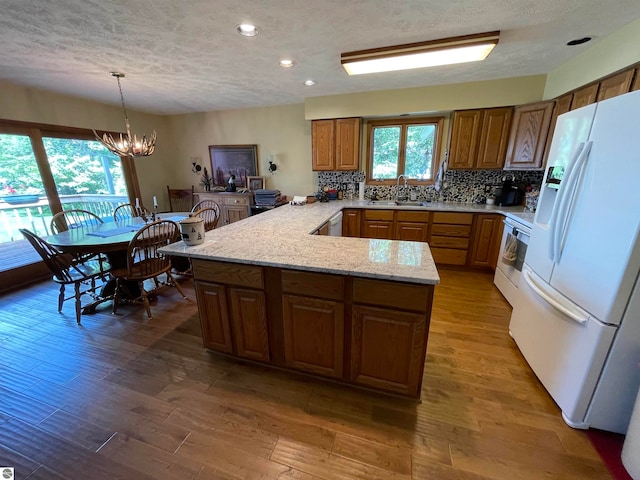 kitchen with white refrigerator, light stone counters, a chandelier, kitchen peninsula, and pendant lighting