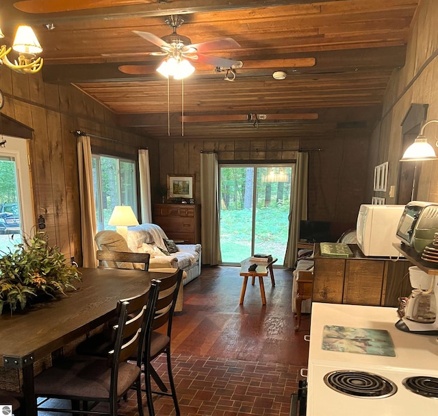 dining room featuring wooden walls, ceiling fan with notable chandelier, and a wealth of natural light