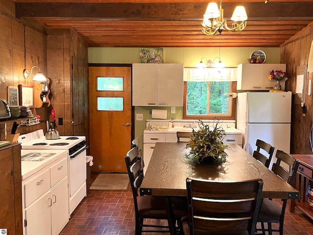 kitchen featuring beamed ceiling, wooden walls, white appliances, white cabinetry, and a chandelier