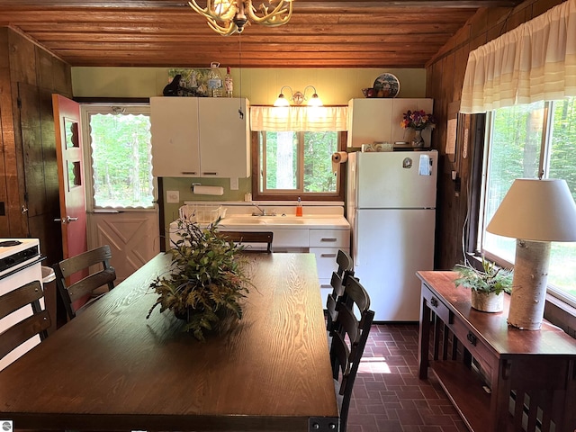 kitchen with a chandelier, wood walls, white fridge, wooden ceiling, and sink