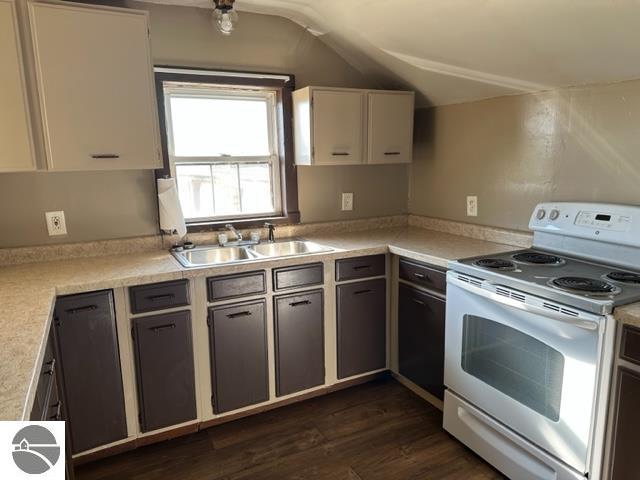 kitchen with dark wood-type flooring, vaulted ceiling, sink, white cabinetry, and electric stove