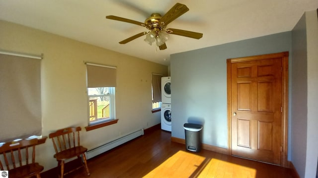 bedroom with dark hardwood / wood-style flooring, ceiling fan, a baseboard radiator, and stacked washer / dryer