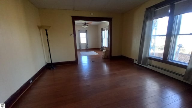 spare room featuring ceiling fan, dark hardwood / wood-style floors, a baseboard heating unit, and a healthy amount of sunlight