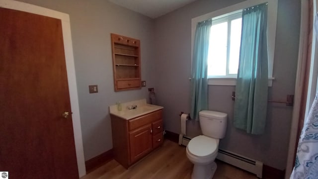 bathroom featuring toilet, vanity, plenty of natural light, and a baseboard heating unit