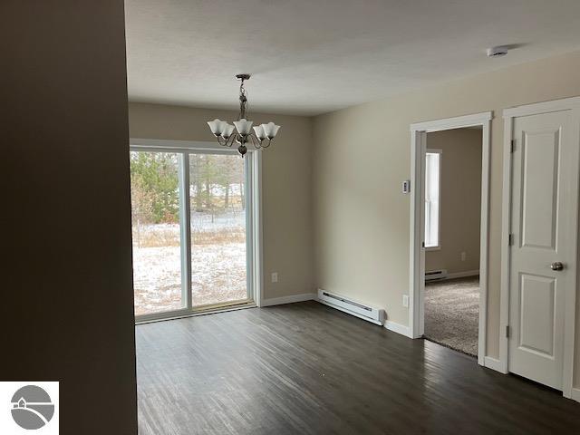 empty room with baseboard heating, dark hardwood / wood-style flooring, plenty of natural light, and an inviting chandelier