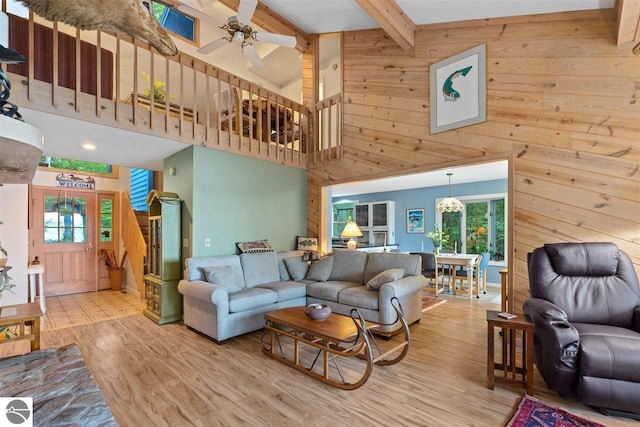 living room featuring beamed ceiling, light hardwood / wood-style floors, wooden walls, ceiling fan, and a high ceiling