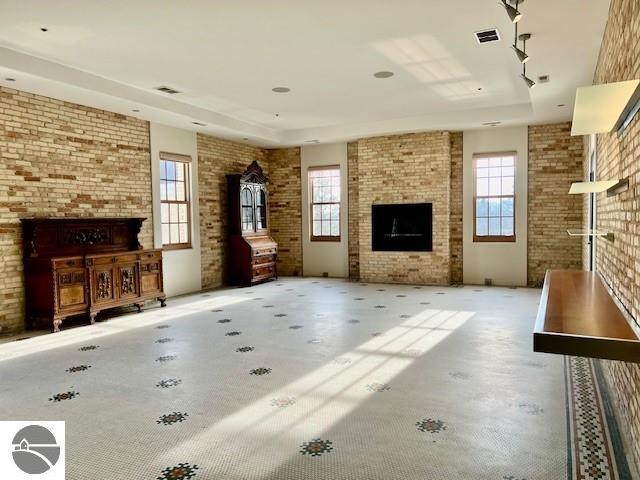 unfurnished living room with a large fireplace, concrete flooring, brick wall, and a raised ceiling