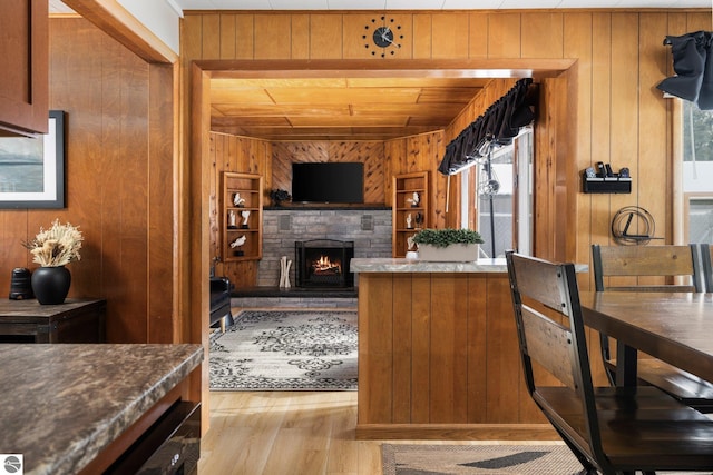 kitchen featuring light hardwood / wood-style floors, wooden walls, and a stone fireplace