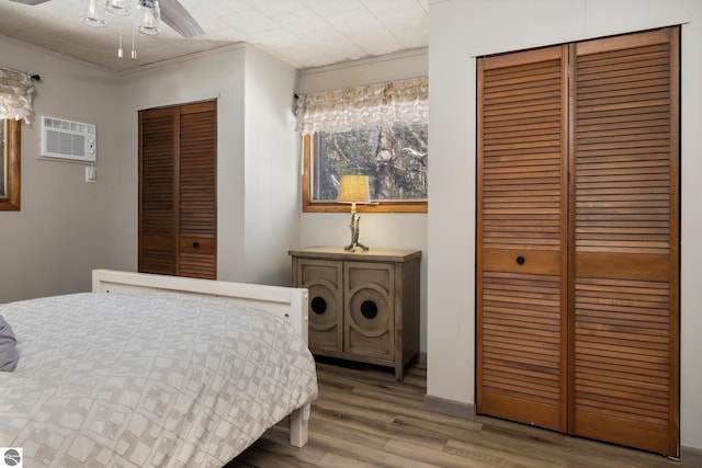 bedroom featuring a wall mounted air conditioner, wood-type flooring, and ceiling fan