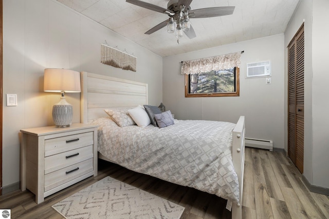 bedroom featuring a closet, ceiling fan, a wall mounted AC, a baseboard radiator, and hardwood / wood-style flooring