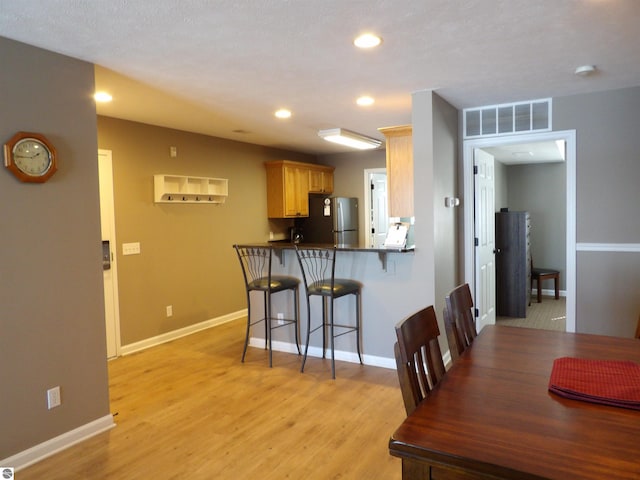 kitchen featuring kitchen peninsula, a breakfast bar area, stainless steel refrigerator, a textured ceiling, and light wood-type flooring