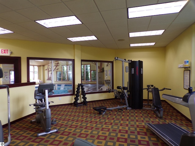 gym with a paneled ceiling and dark colored carpet