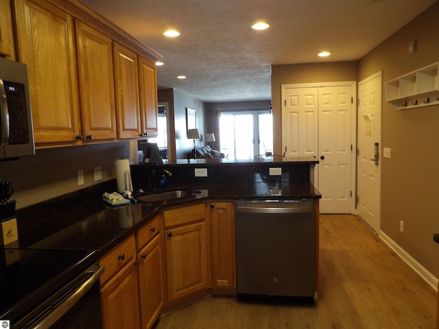 kitchen with stainless steel appliances, a textured ceiling, light hardwood / wood-style flooring, dark stone countertops, and sink