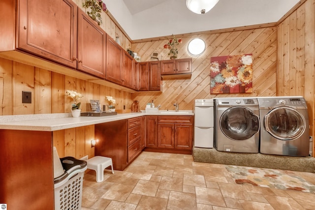 clothes washing area featuring wood walls, light tile patterned flooring, washer and clothes dryer, and sink