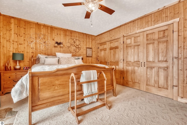 carpeted bedroom with ceiling fan, a textured ceiling, and wooden walls