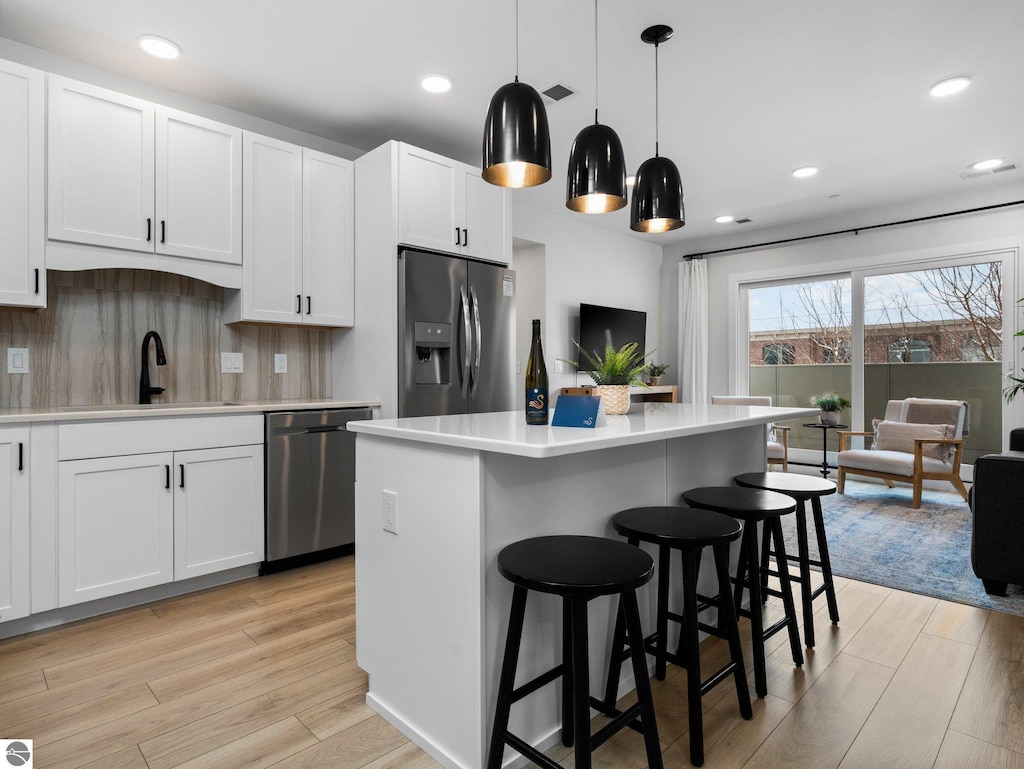 kitchen with light hardwood / wood-style flooring, decorative light fixtures, appliances with stainless steel finishes, and white cabinetry