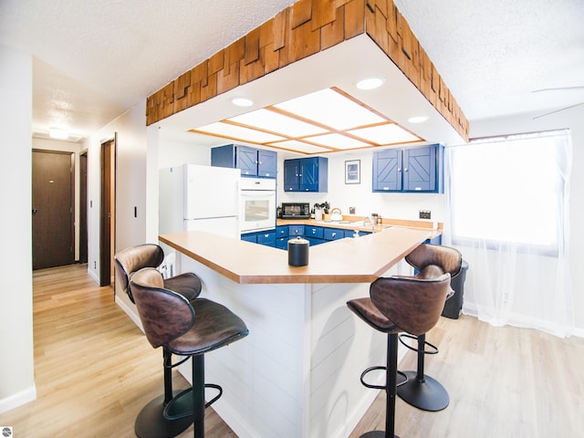 kitchen with a kitchen breakfast bar, a textured ceiling, blue cabinets, and light hardwood / wood-style flooring