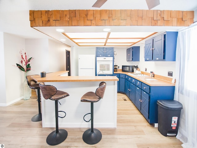 kitchen featuring white appliances, blue cabinets, a breakfast bar, and light wood-type flooring