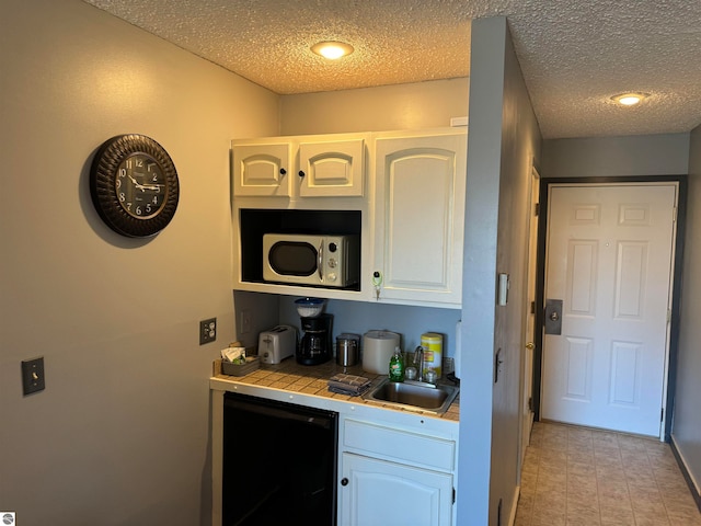 bar with tile countertops, white cabinets, dishwasher, and a textured ceiling