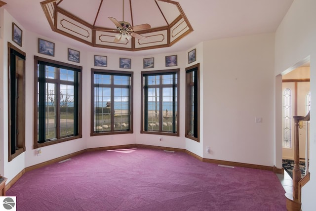 carpeted spare room with plenty of natural light, a raised ceiling, and ceiling fan