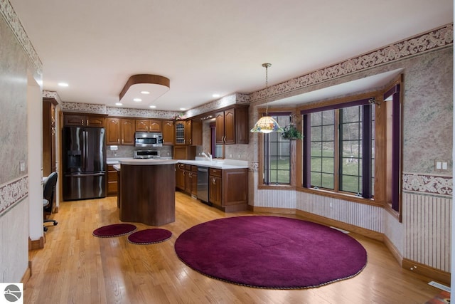 kitchen with pendant lighting, light wood-type flooring, backsplash, appliances with stainless steel finishes, and a kitchen island