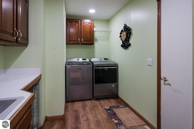 clothes washing area with wood-type flooring, washing machine and dryer, and cabinets