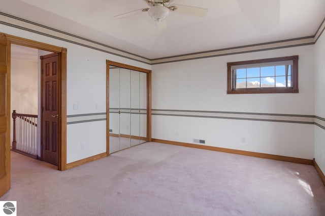 empty room with a raised ceiling, ceiling fan, and light carpet