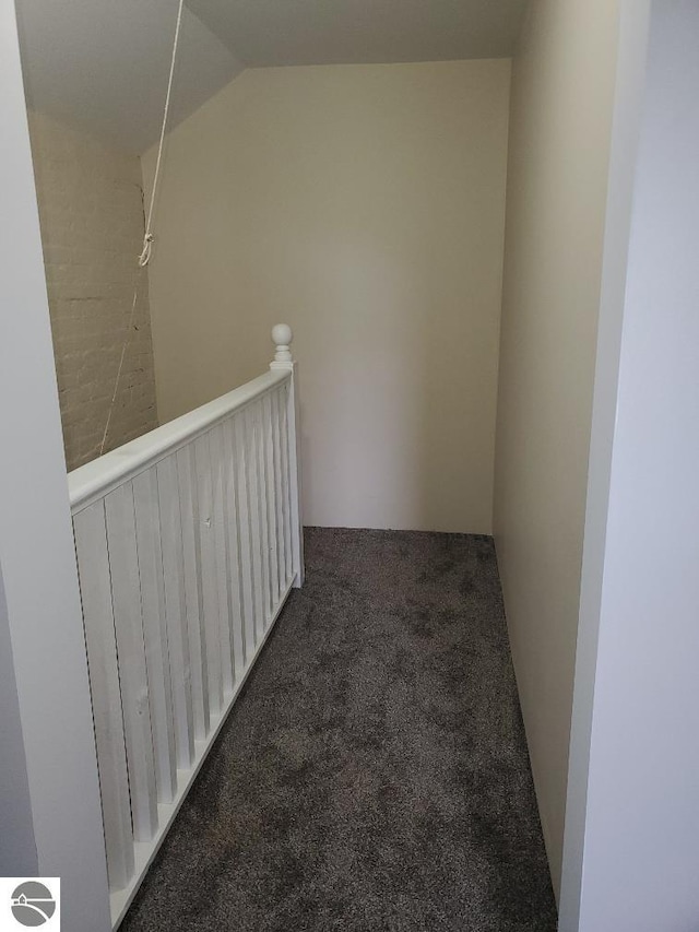 hallway with dark colored carpet and lofted ceiling