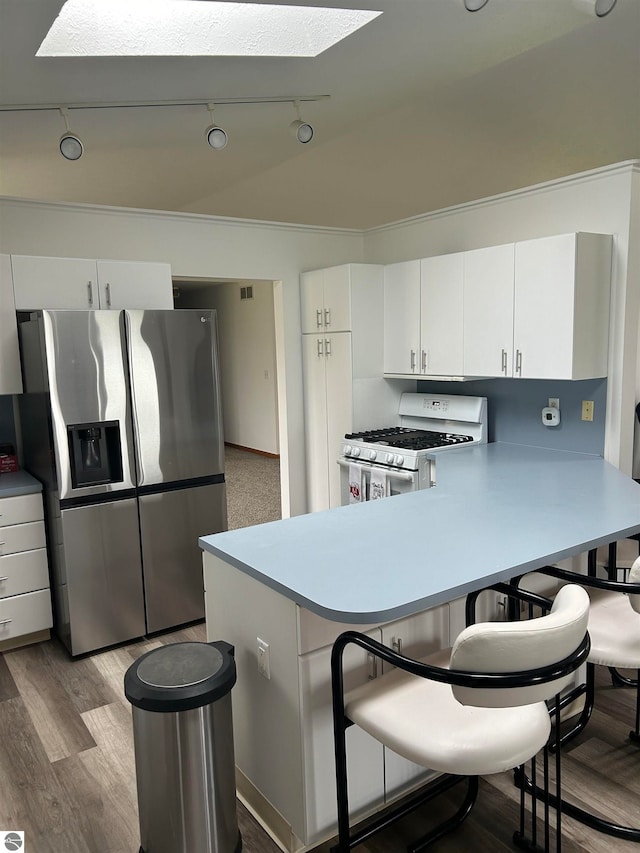 kitchen with track lighting, kitchen peninsula, stainless steel fridge with ice dispenser, white gas range, and white cabinetry