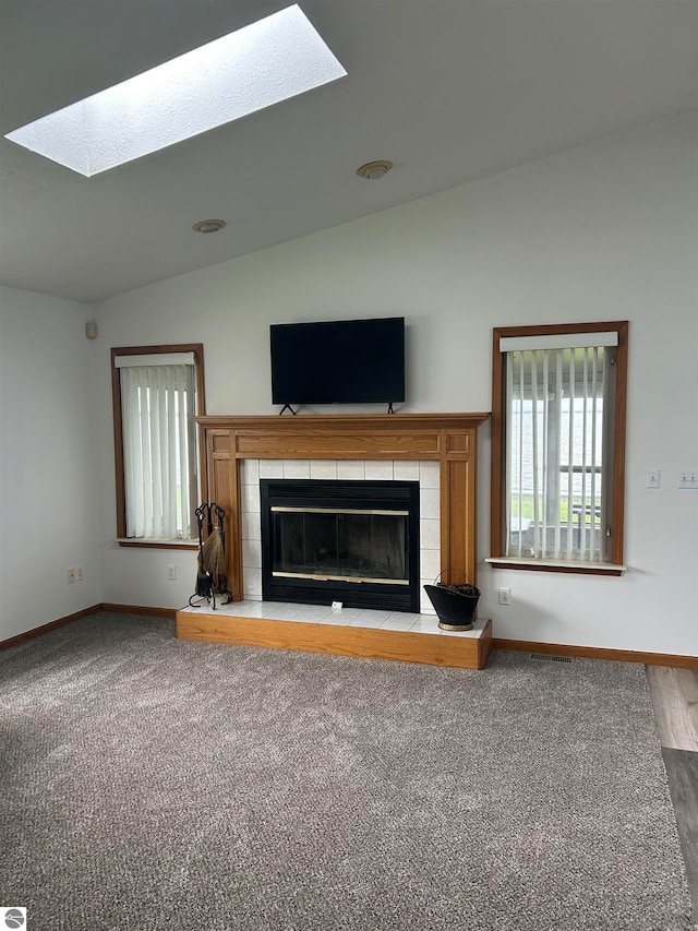 unfurnished living room featuring lofted ceiling with skylight, a fireplace, and carpet floors