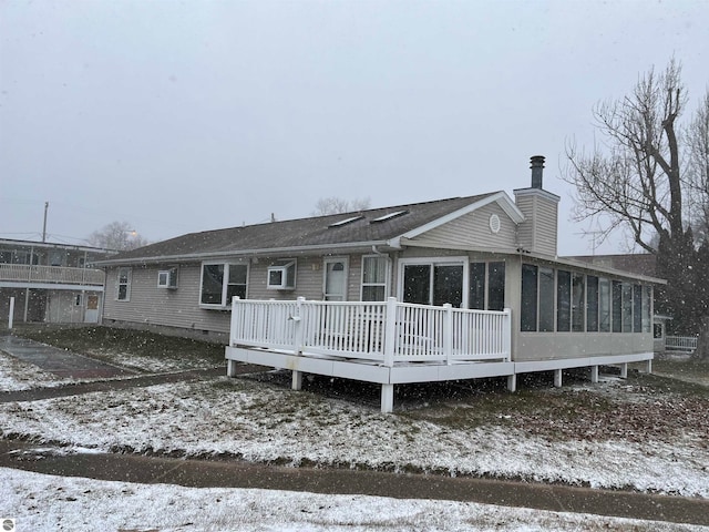 snow covered back of property featuring a wooden deck and a sunroom