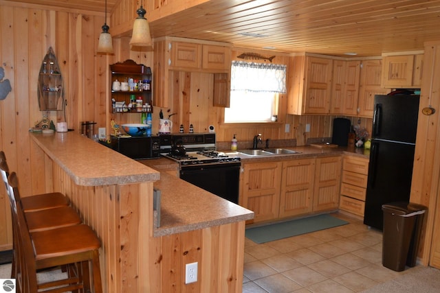 kitchen featuring wooden walls, black refrigerator, decorative light fixtures, white gas stove, and sink