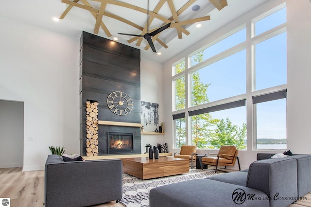 living room featuring beamed ceiling, ceiling fan, a towering ceiling, a tiled fireplace, and light hardwood / wood-style flooring