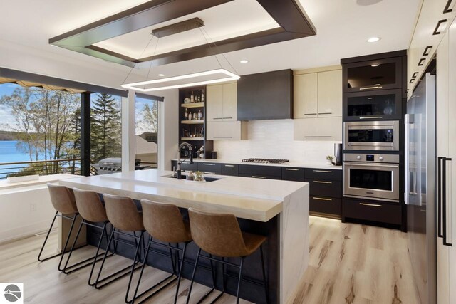 kitchen featuring appliances with stainless steel finishes, tasteful backsplash, sink, light wood-type flooring, and a raised ceiling