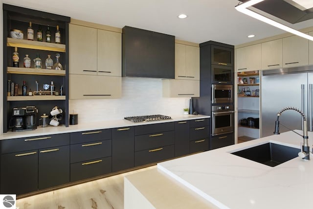 kitchen with light stone counters, sink, light hardwood / wood-style floors, backsplash, and built in appliances