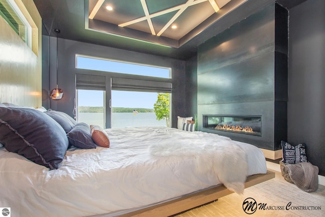 bedroom with a large fireplace, a water view, hardwood / wood-style flooring, and a tray ceiling