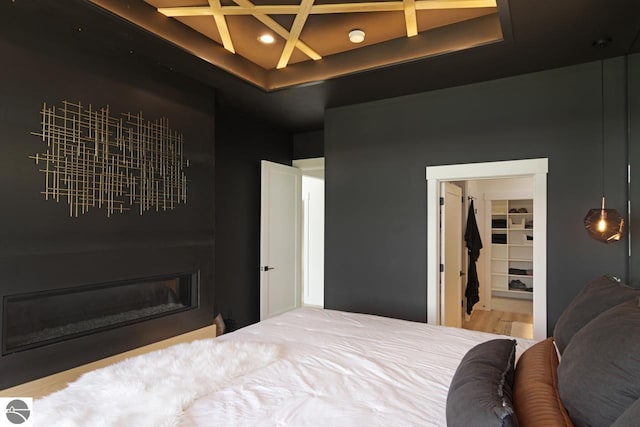 bedroom featuring a spacious closet, wood-type flooring, a tray ceiling, and coffered ceiling